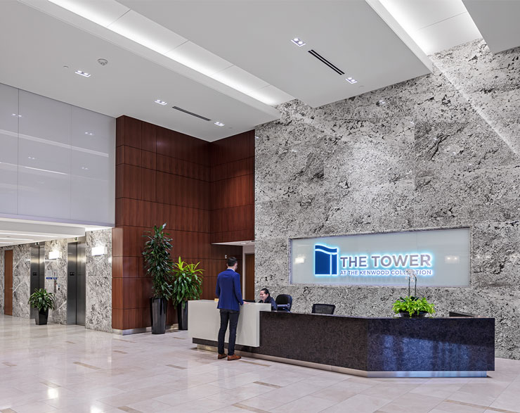 A receptionist desk is backed by a floor-to-ceiling granite wall